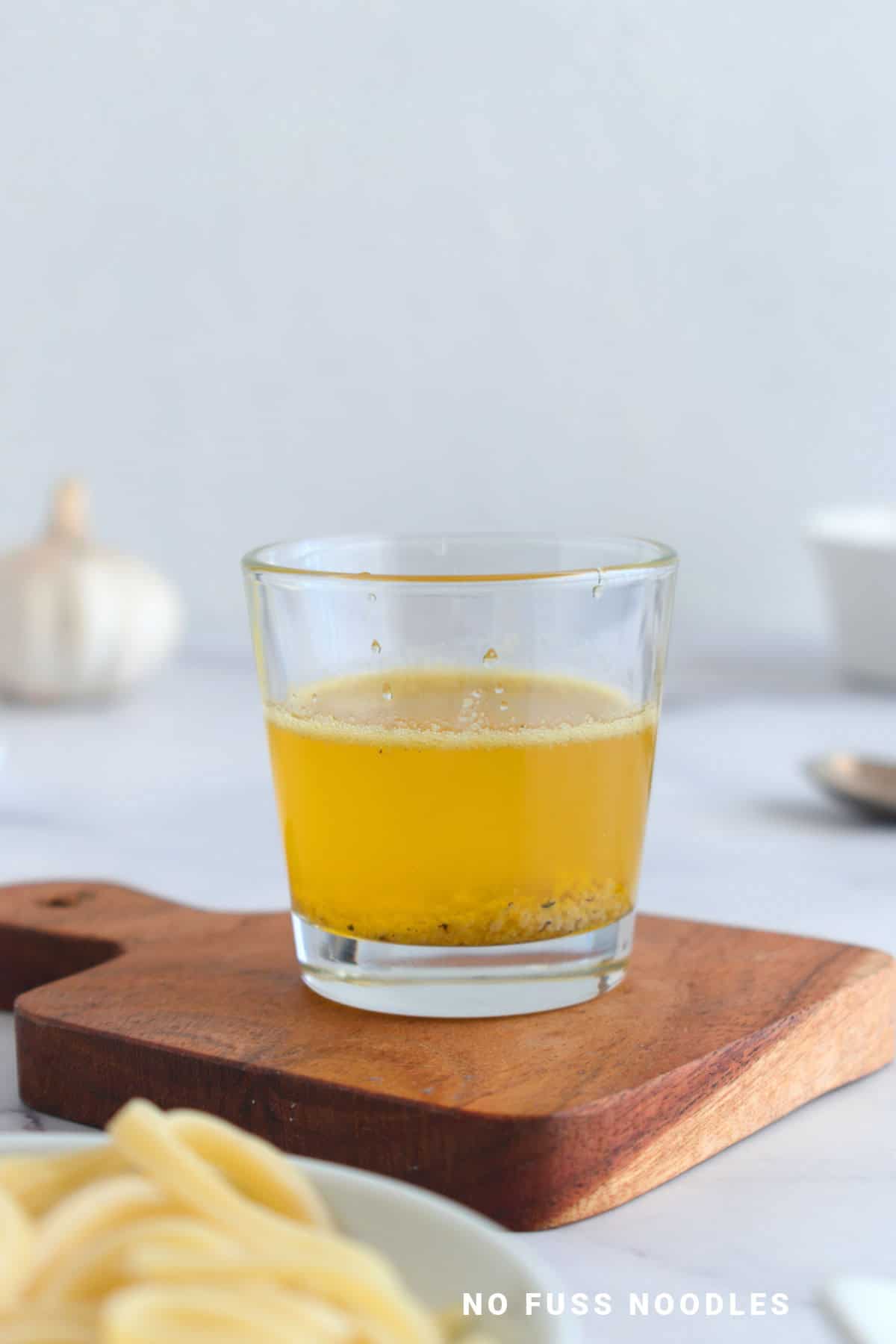 Garlic butter sauce in a glass on a wooden board.