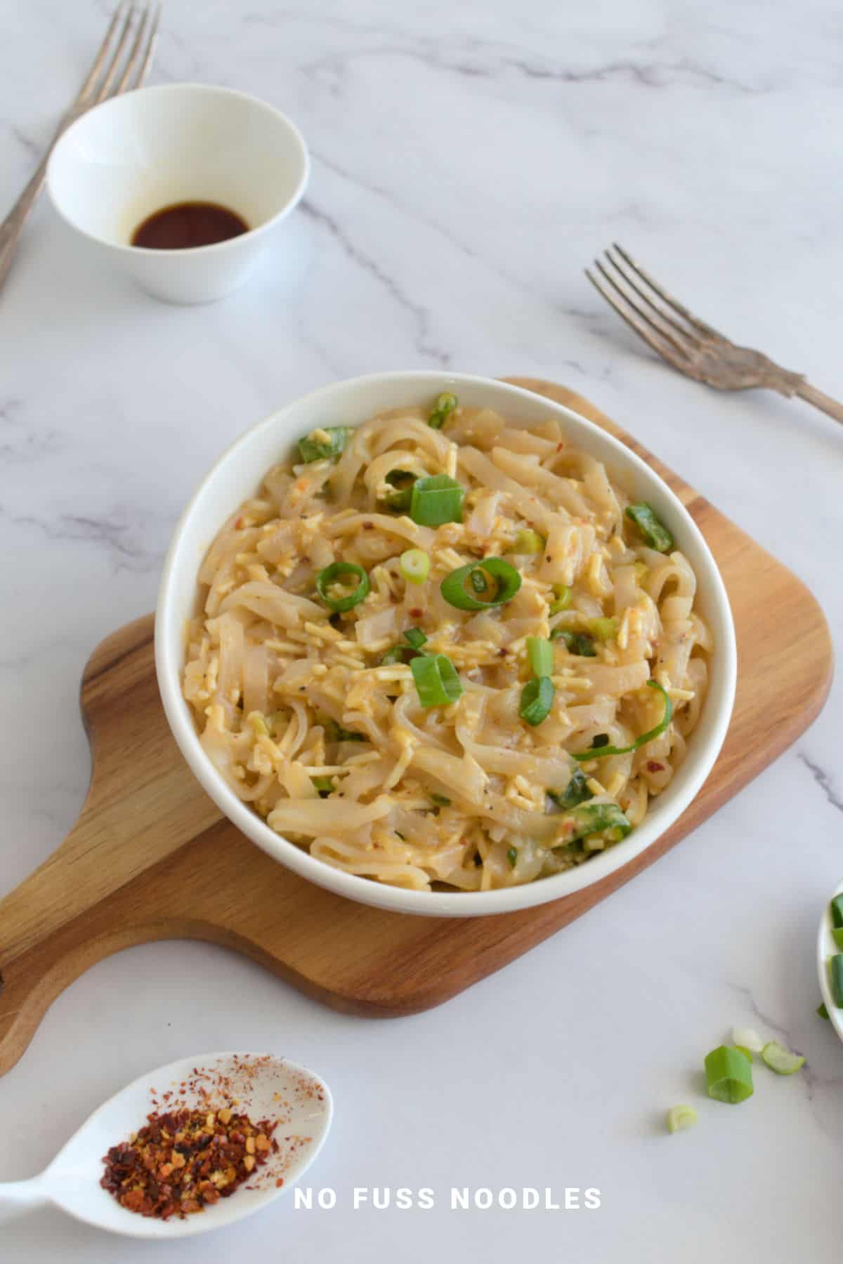 Hot garlic noodles in a white bowl on a wooden board.