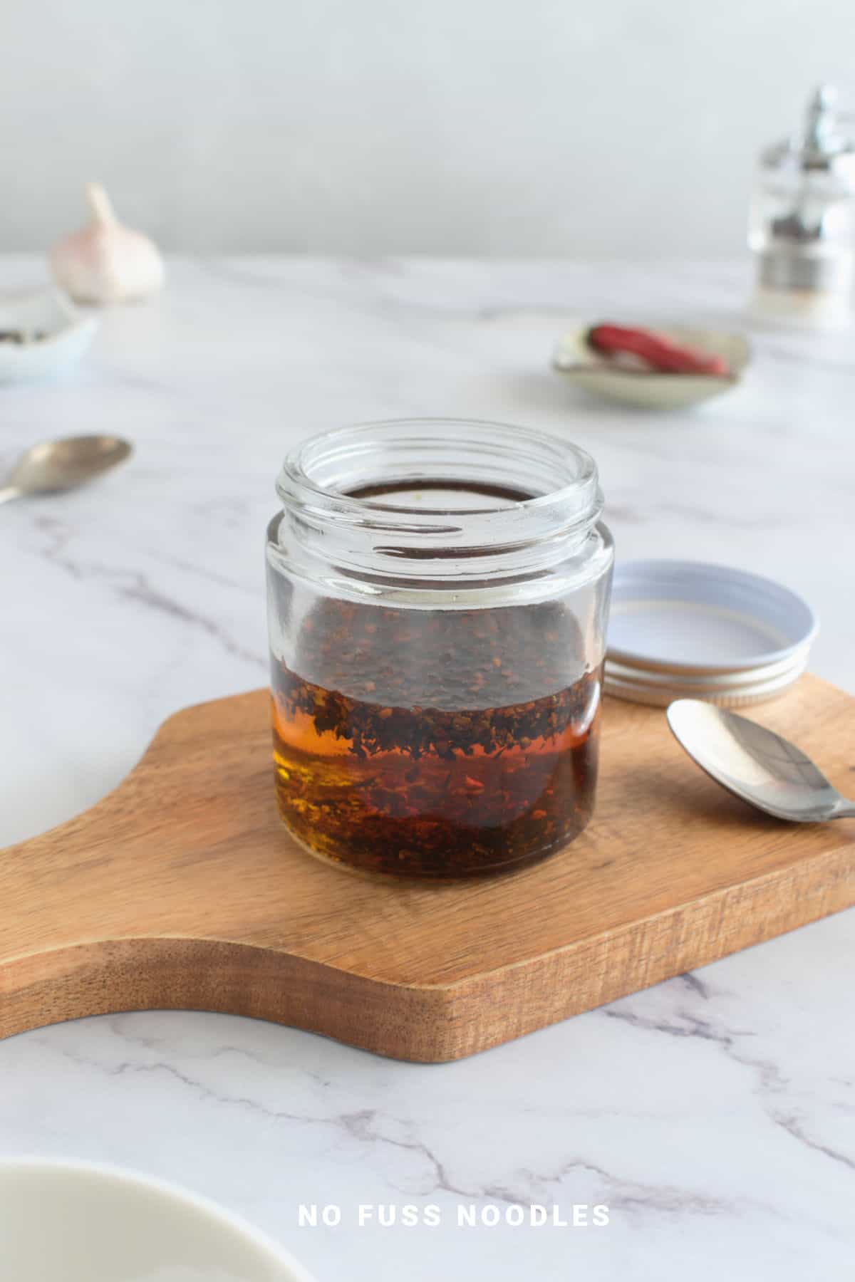 Chili oil in a jar on a wooden board.