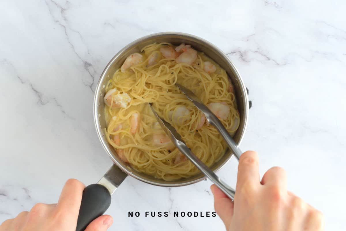 Tossing pasta through garlic lemon sauce in a saucepan.